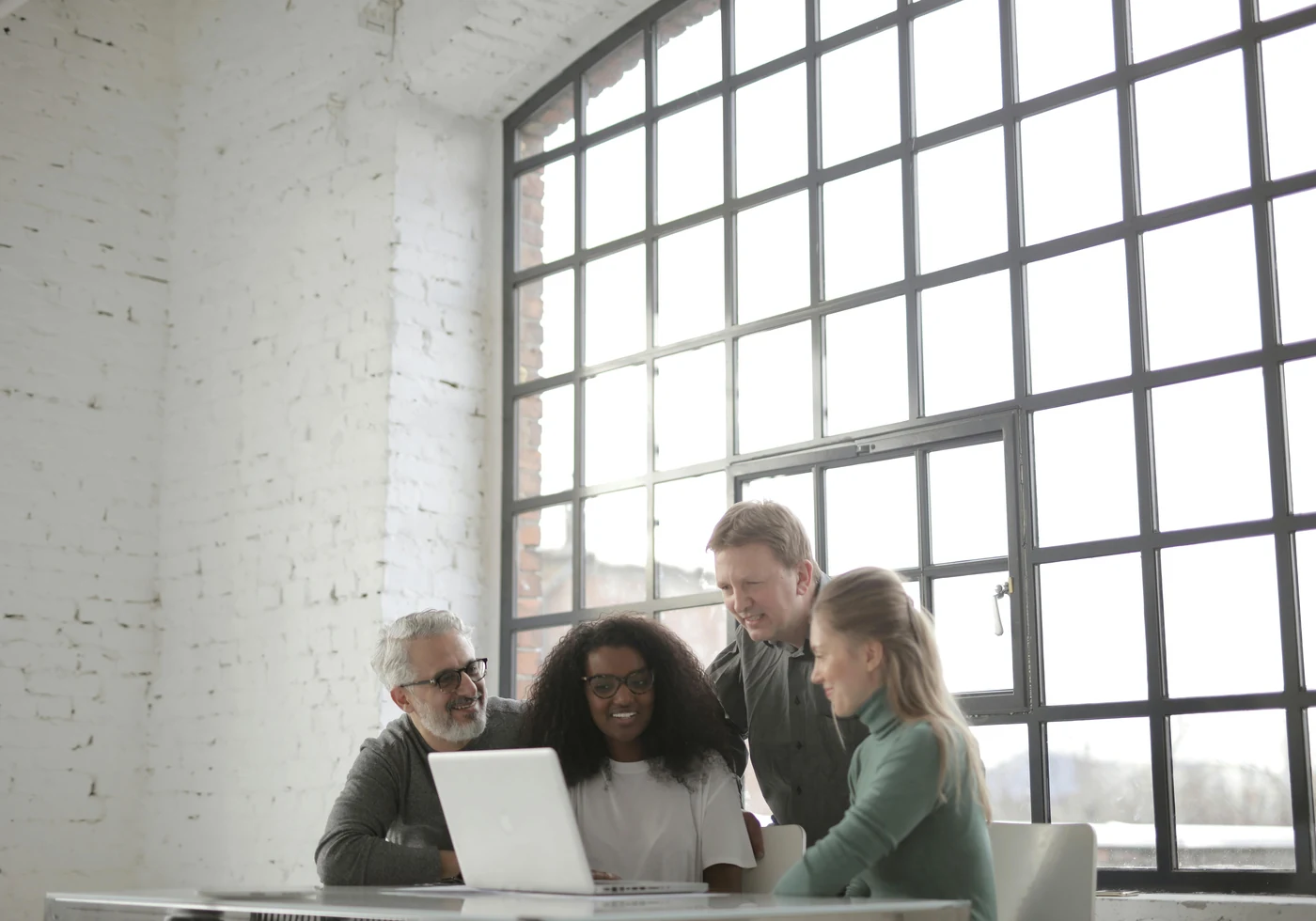 A diverse team collaborating around a laptop in a bright workspace